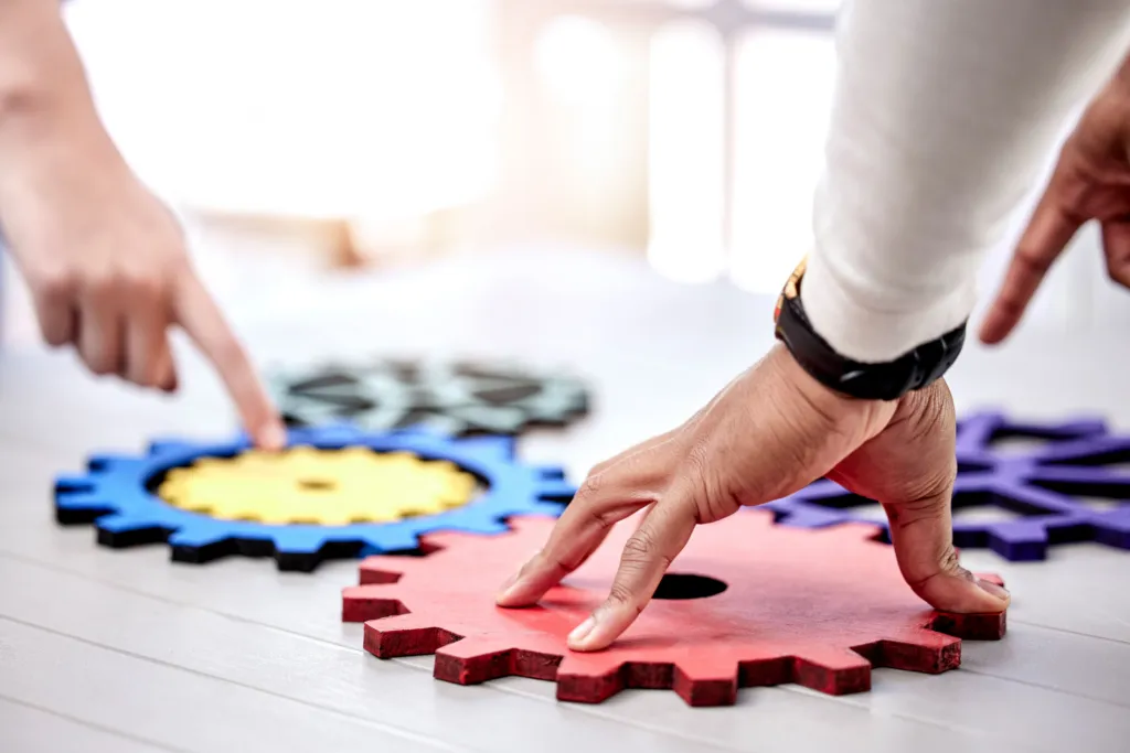Close-up shot of a diverse business team connecting wooden gear cogs in a circle, symbolizing innovation and teamwork