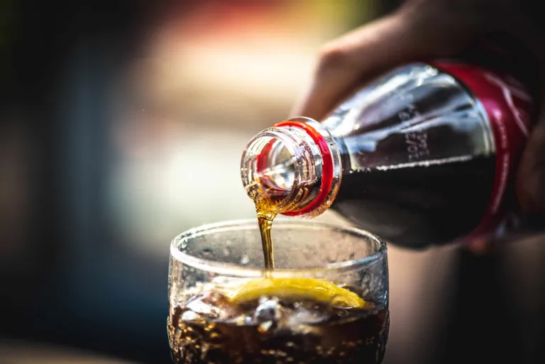 Refreshing beverage being poured into a clear glass filled with ice cubes and sliced fresh lemon