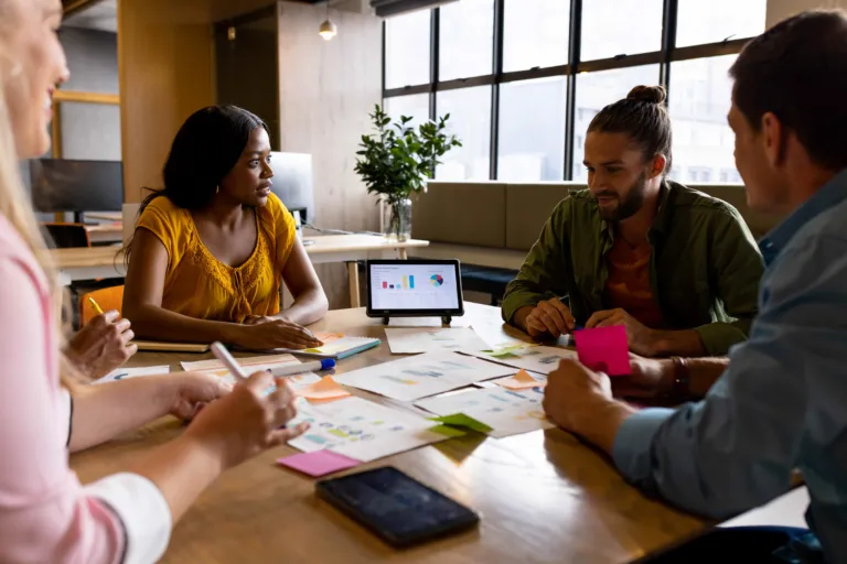 Diverse group of business professionals sitting around a table collaborating and reviewing printed graphs and charts