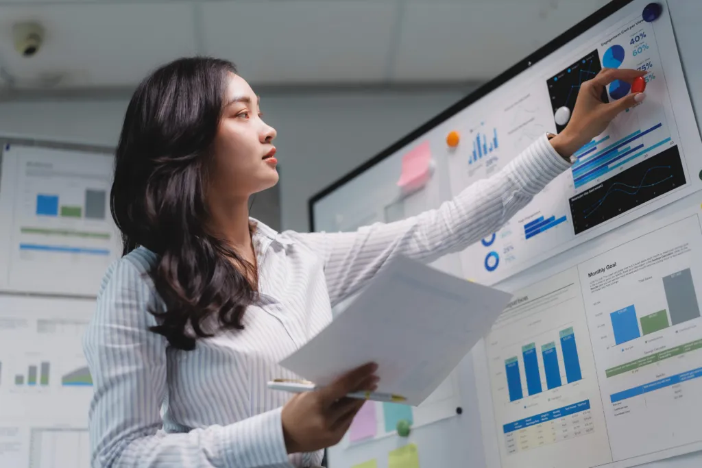 Professional businesswoman standing and presenting financial data and charts to colleagues in a modern office meeting room
