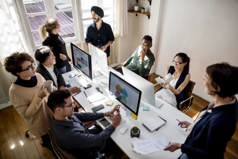 Diverse group of eight multicultural professionals working together on computers in a modern office